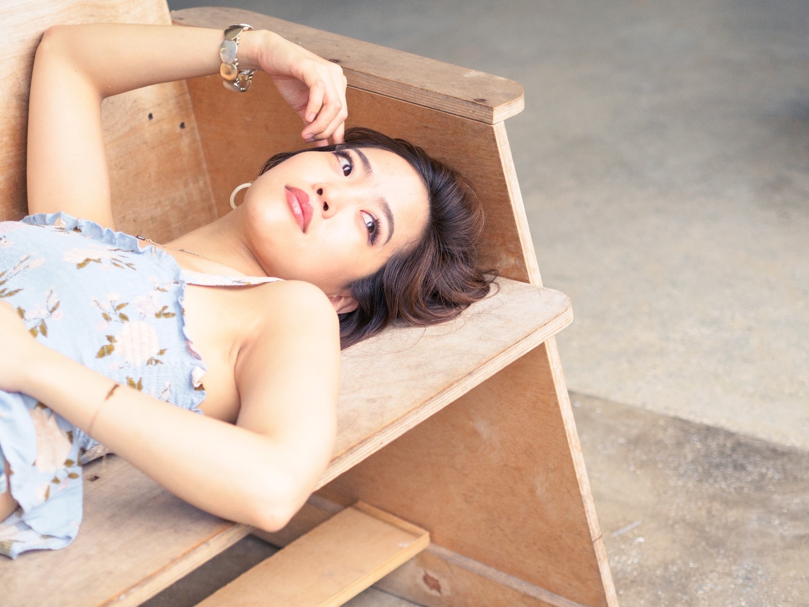 A young woman with short hair lies on a wooden bench outdoors.