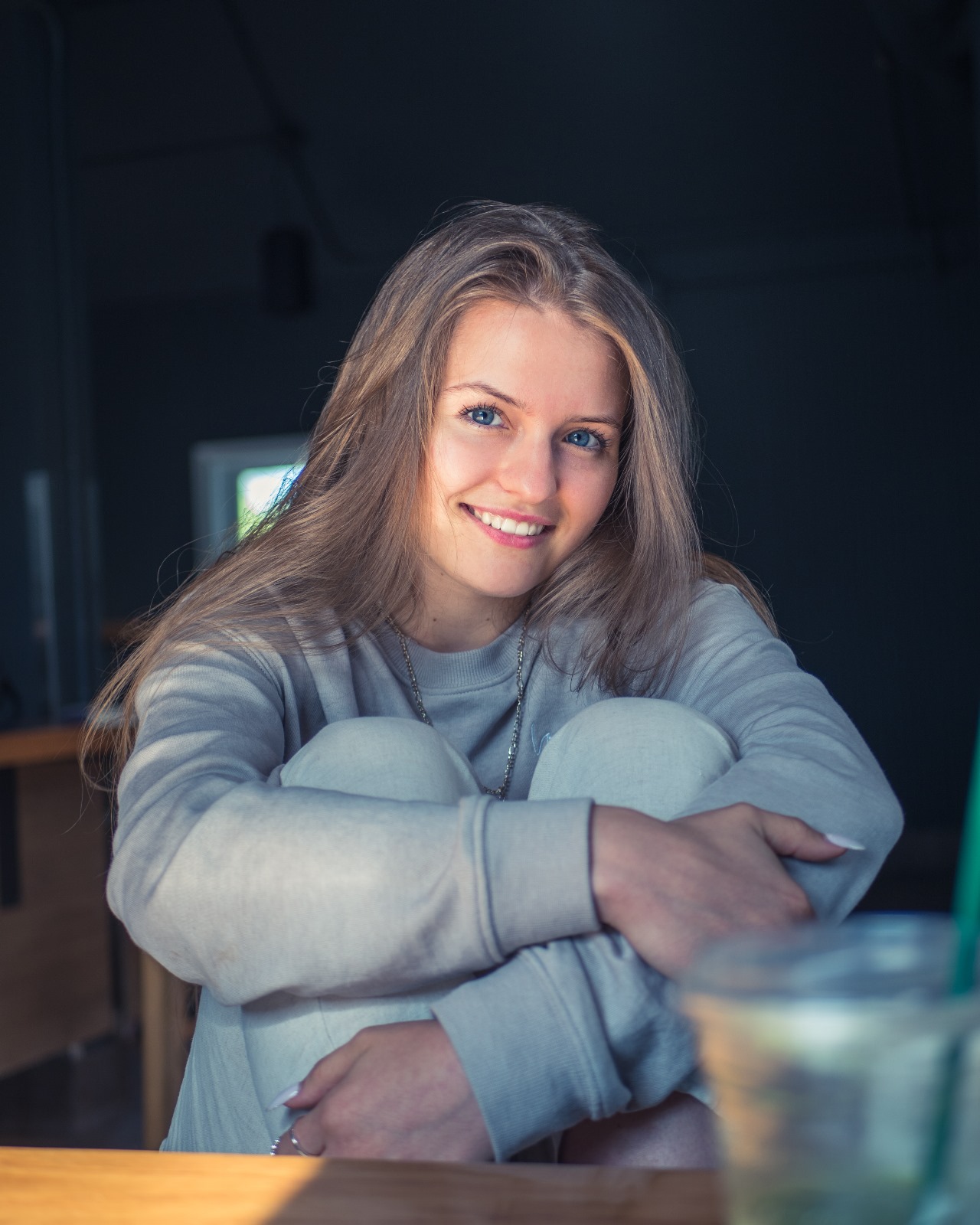 A smiling woman sitting against a table with her arms crossed in a coffee shop.